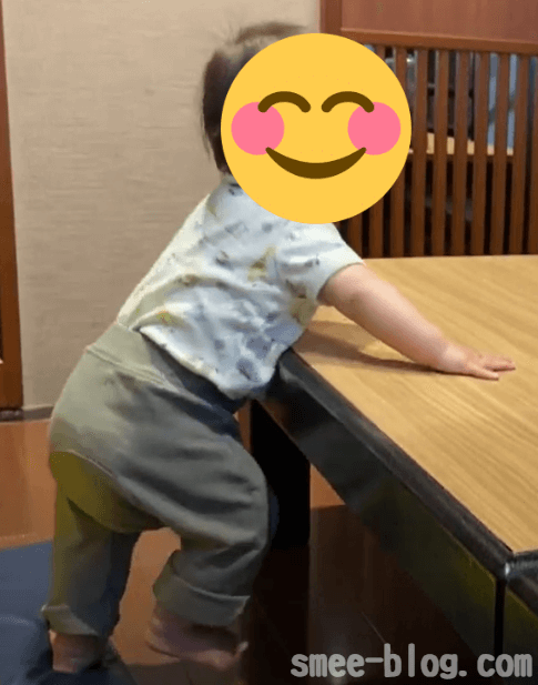赤ちゃんがテーブルに手をついて立ち、片足を上げて横に移動している様子