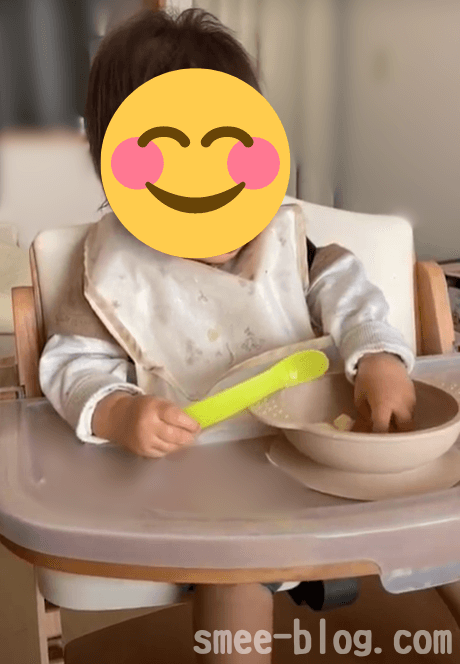赤ちゃんが片手にスプーンを持ちながら離乳食を食べている